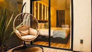 A bedroom with a large sliding glass door, a wicker chair, and a bed with a blue blanket. - Nowness (Mexico City)