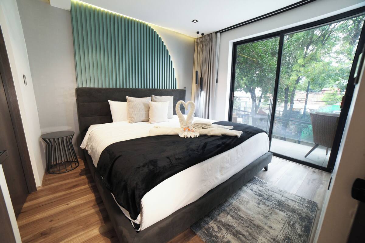 Un dormitorio moderno con una cama grande, una mesita redonda y vistas al exterior a través de un amplio ventanal.
