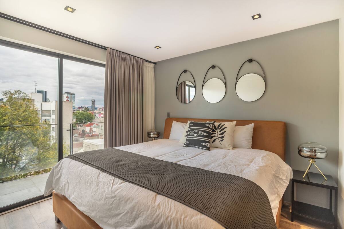 Un dormitorio moderno con una cama grande, dos mesitas de noche y tres espejos adosados a la pared.