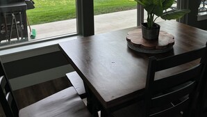 A dining area with a table and chairs, a potted plant, and a view of a grassy yard and mountains through large windows.