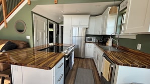 A modern kitchen with white cabinets, a stainless steel refrigerator, and a wooden countertop.