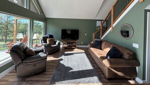 A spacious living room with a large window, a flat-screen TV, and a staircase.