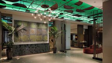 A modern lobby with a green-lit ceiling, a large abstract art display, and a seating area with a red sofa.