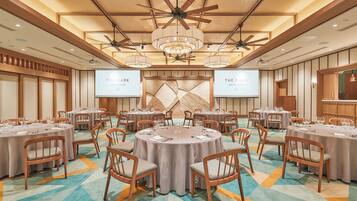Ein Konferenzraum mit runden Tischen, Stühlen und einem großen Bildschirm, der "THE MARRIOTT GRAND HOTEL" anzeigt.