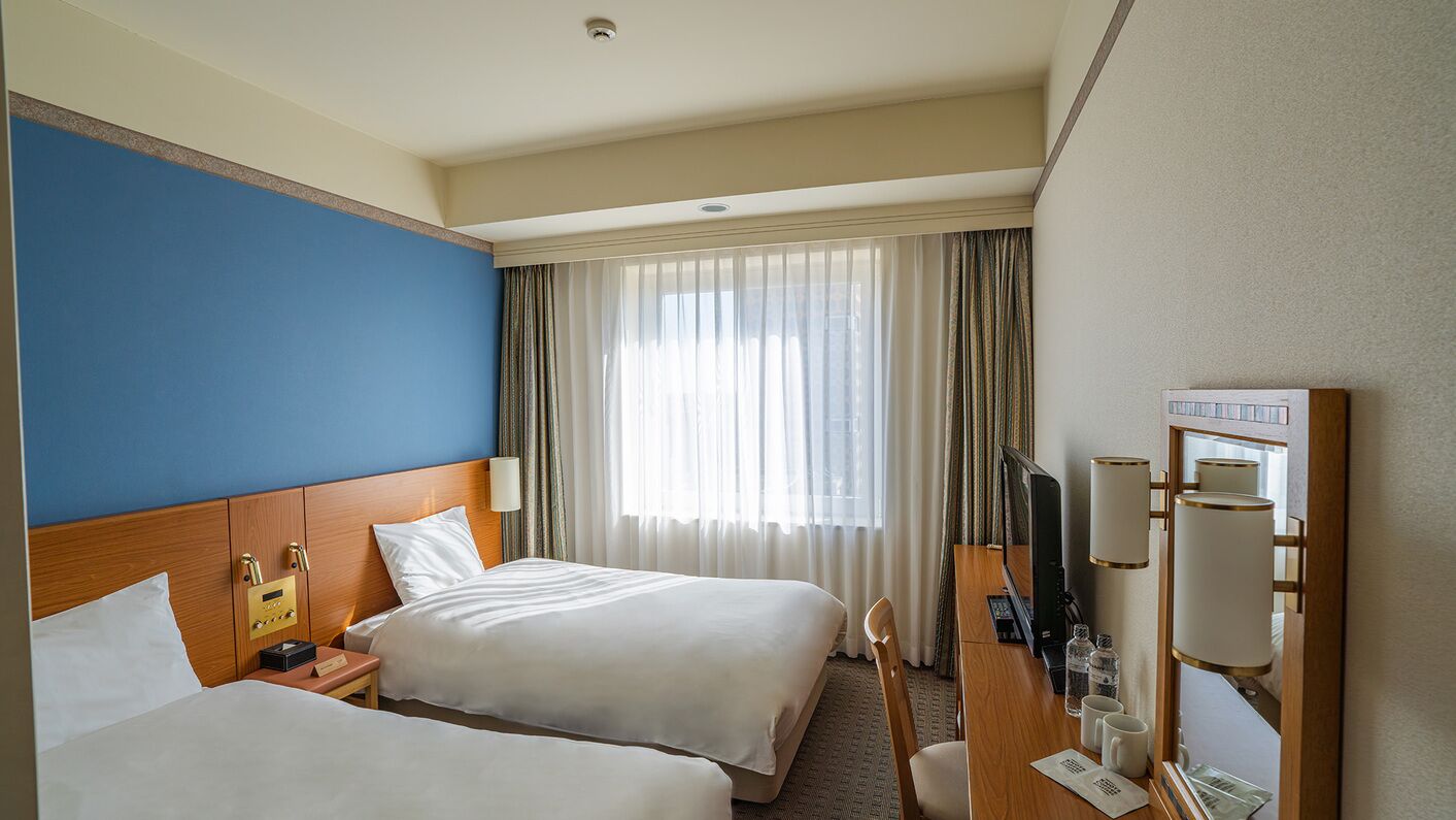 Ein Hotelzimmer mit zwei Betten, einem Schreibtisch mit Computer, Fernseher und einer Minibar.