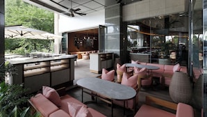 Un área de estar exterior moderna con barra, sofás acolchados y una pared de cristal con vistas a un jardín.