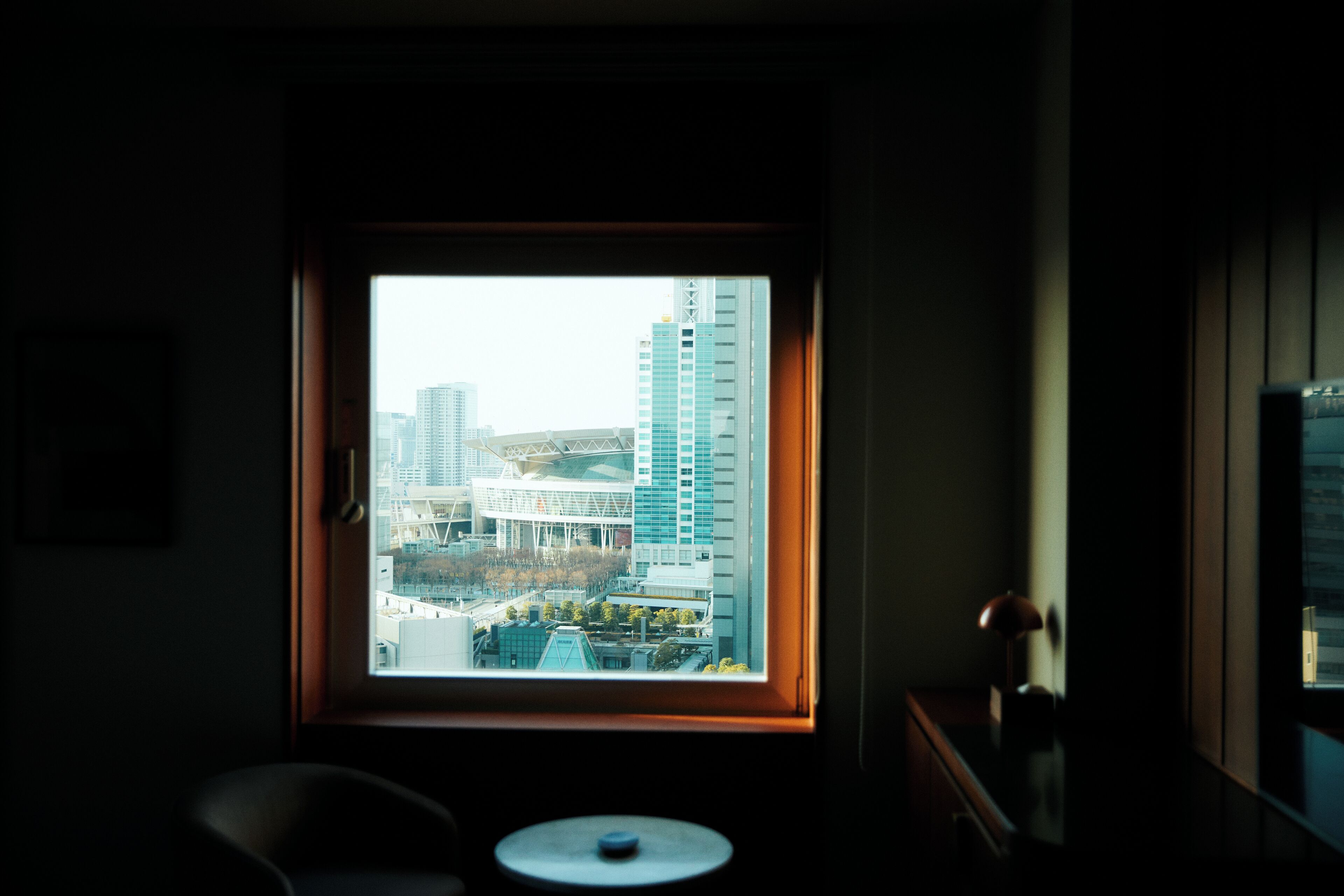 A room with a large window overlooking a cityscape, a small round table, and a chair.