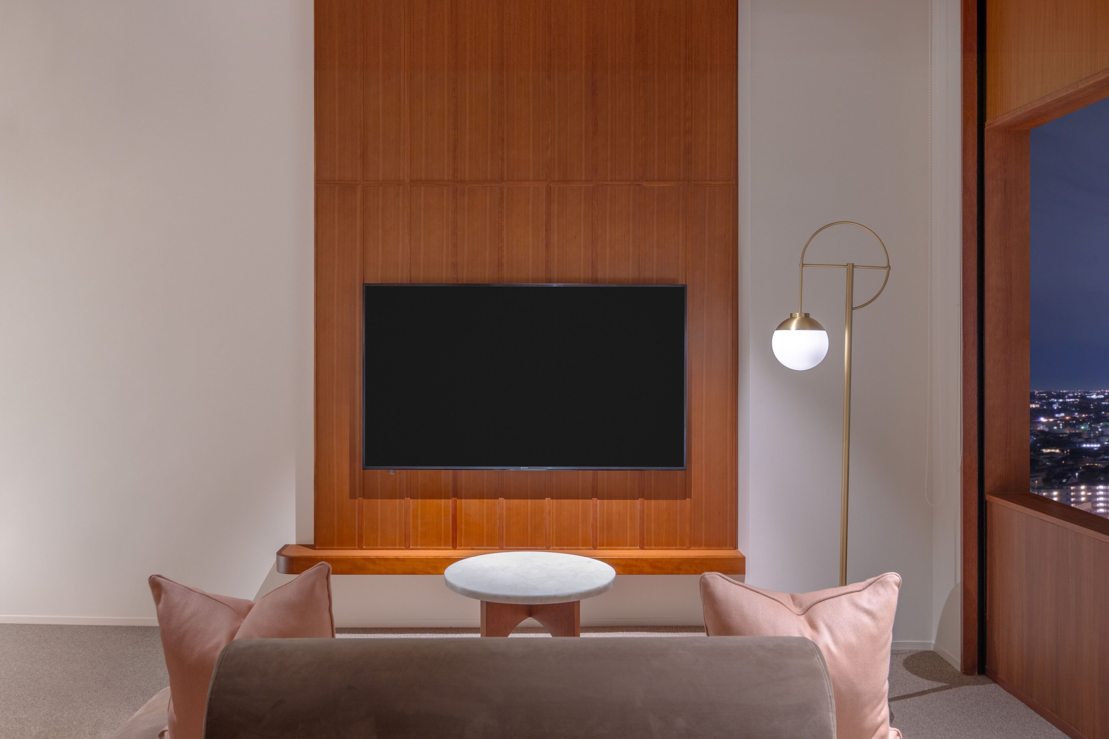 A modern living room with a large flat-screen TV mounted on a wooden wall, a round white table, and a floor lamp.