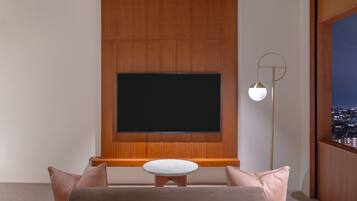 A modern living room with a large flat-screen TV mounted on a wooden wall, a round white table, and a floor lamp.