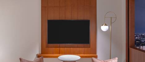 A modern living room with a large flat-screen TV mounted on a wooden wall, a round white table, and a floor lamp.