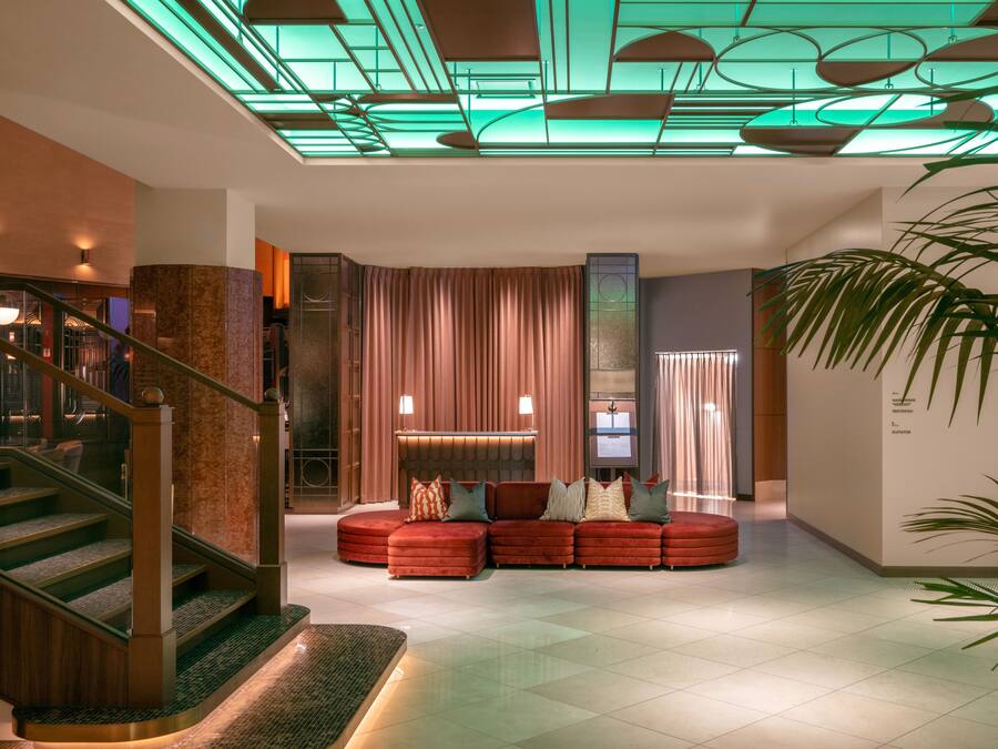 A modern lobby with a curved red sofa, a staircase, and a glass ceiling.