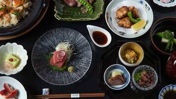 Verschiedene japanische Gerichte auf einem Tisch, darunter Sushi, Sashimi und weitere Köstlichkeiten, mit Stäbchen und kleinen Sojasaucenschälchen.