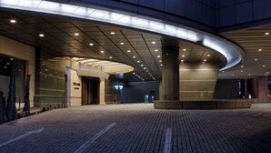 Un edificio moderno con una entrada curva, una plaza pavimentada y una serie de luces en el techo.