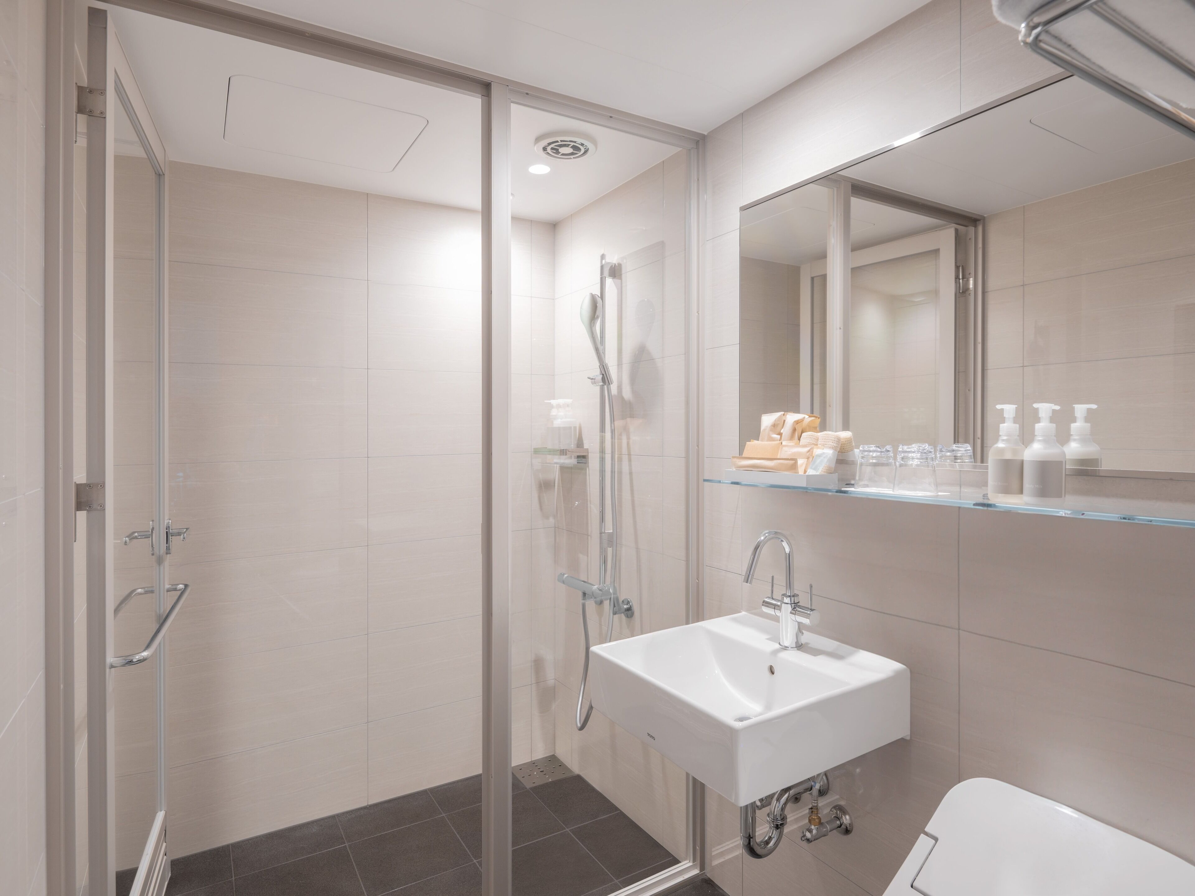Un baño moderno con cabina de ducha de vidrio, un lavabo blanco y un espejo encima.