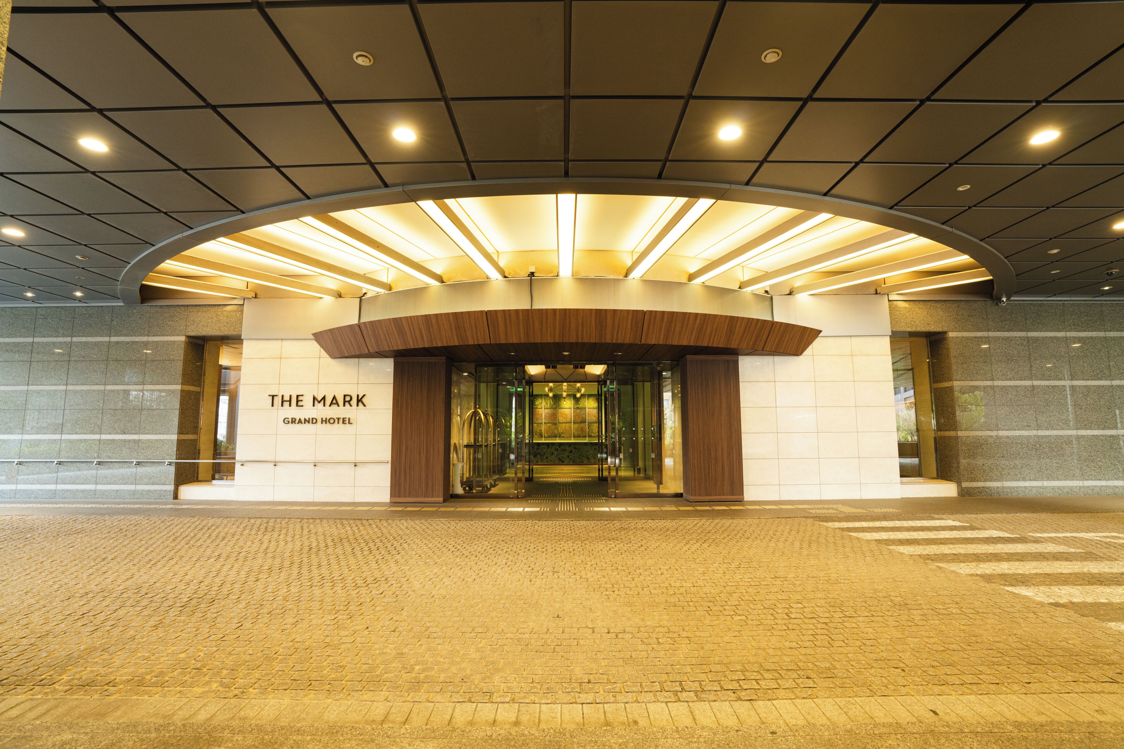 A hotel entrance with a curved canopy, glass doors, and a sign reading 'The Mark Grand Hotel.'