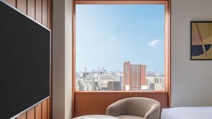Una habitación de hotel con un ventanal grande, una cama, una silla y una mesita.