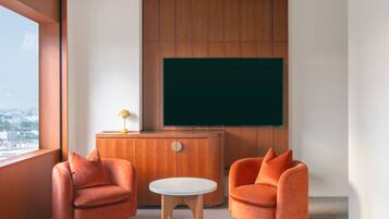 A modern room with two orange armchairs, a small round table, and a wooden cabinet with a television mounted on the wall.