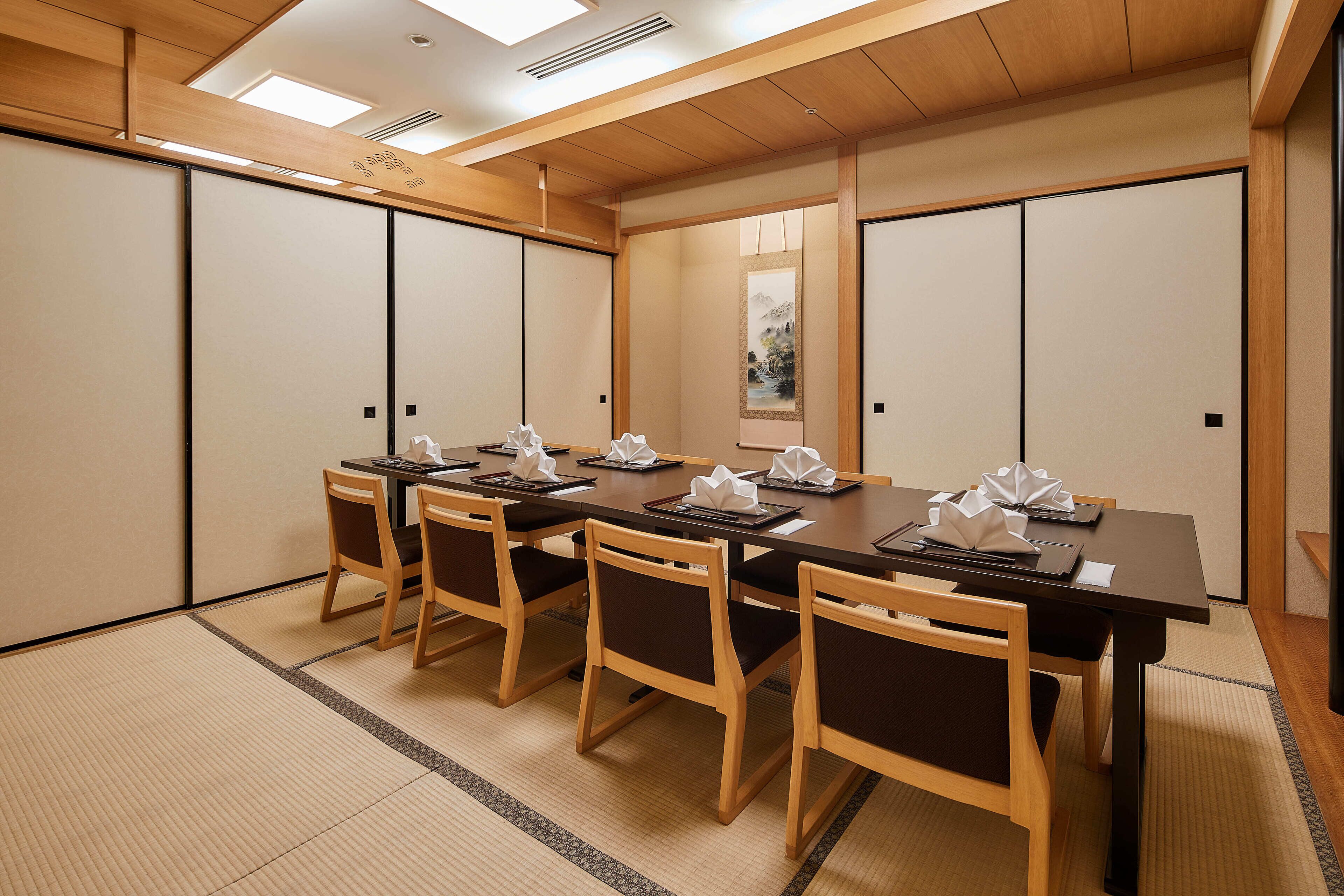 Una sala de reuniones tradicional japonesa con suelo de tatami, mesas y sillas de madera.