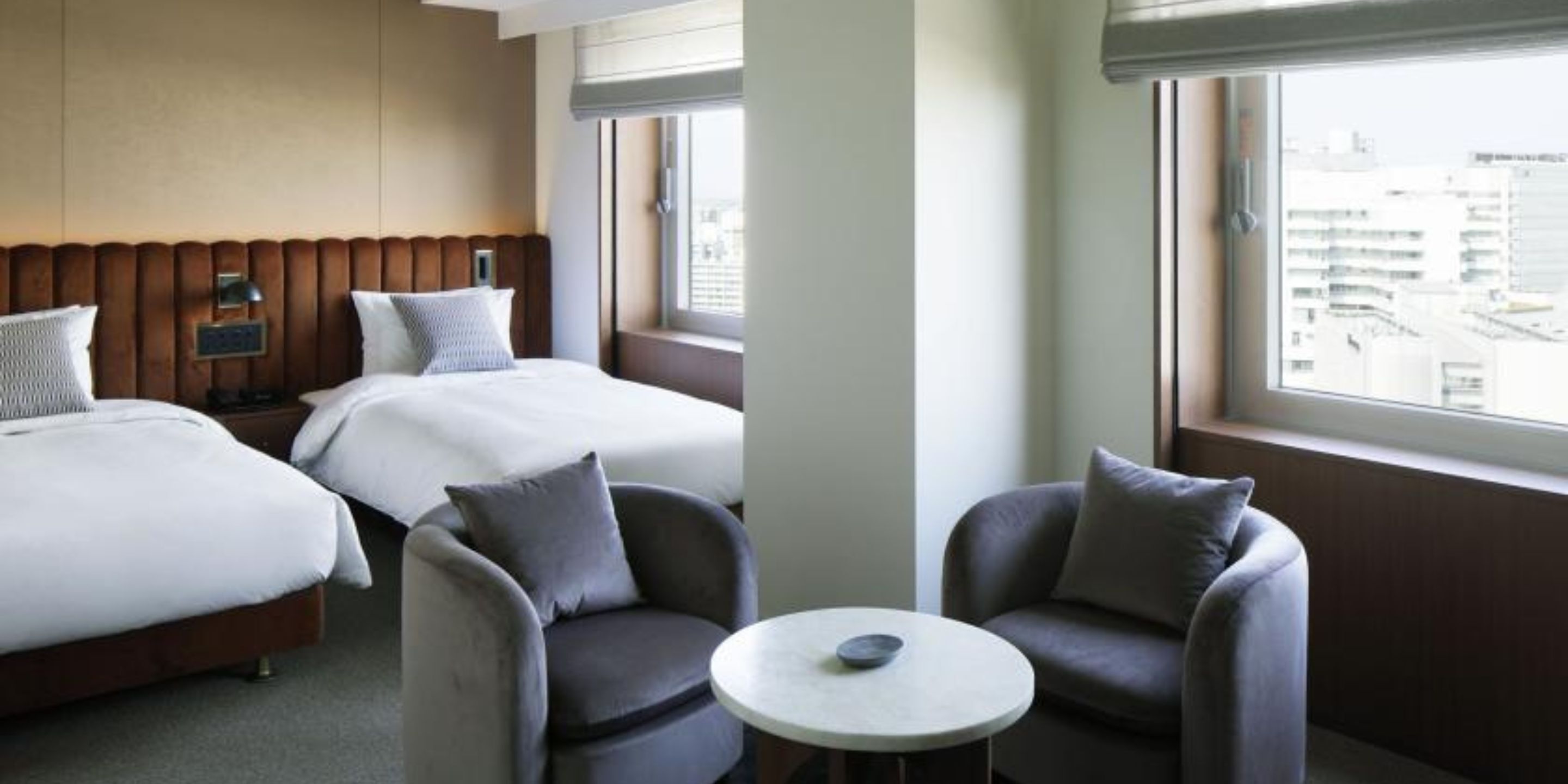 A hotel room with two beds, a small round table, and two armchairs.