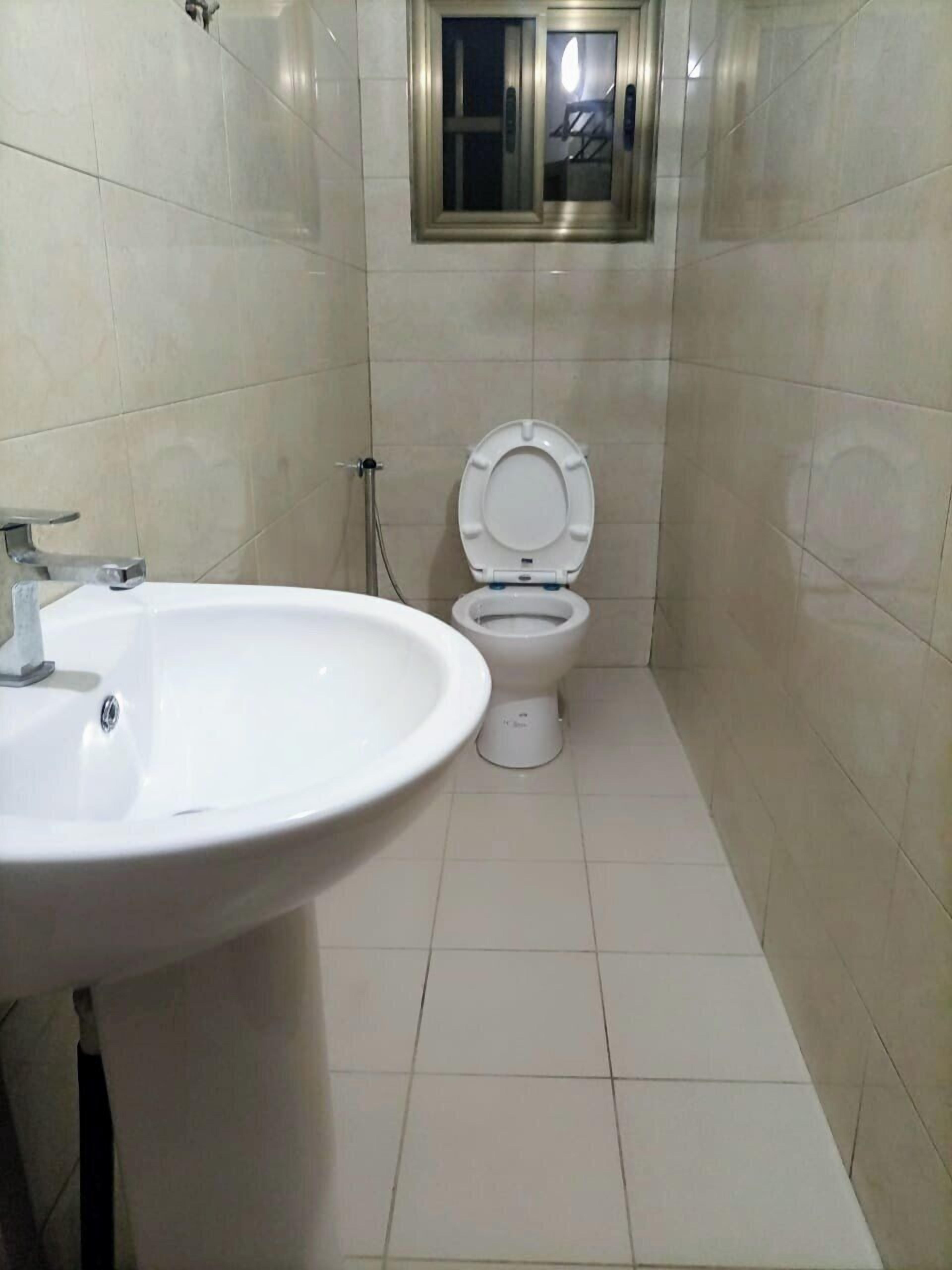 Bagno con lavandino bianco, water e una piccola finestra sopra il water.