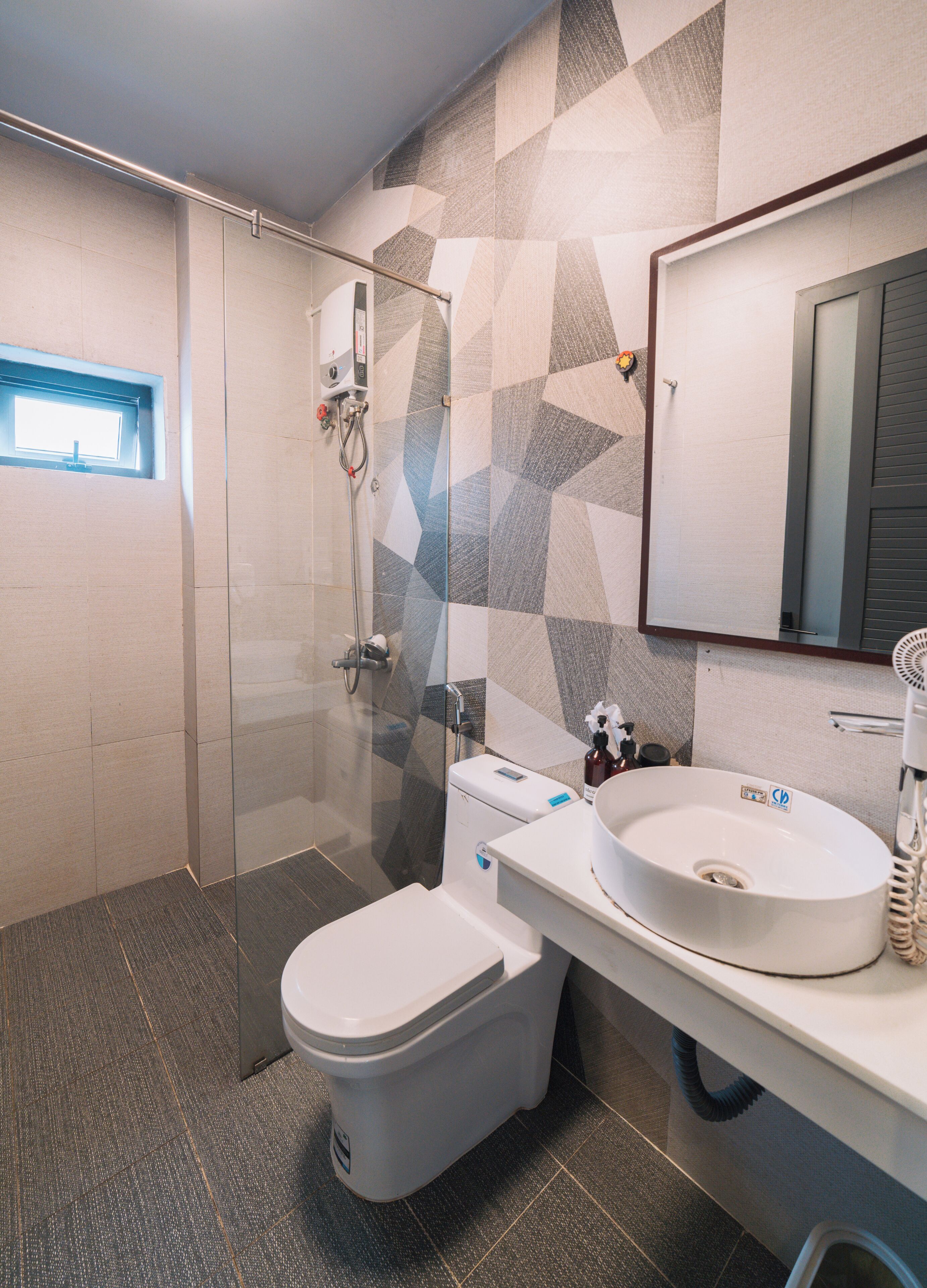 A modern bathroom with a glass shower enclosure, a toilet, a sink with a mirror, and a patterned wall.