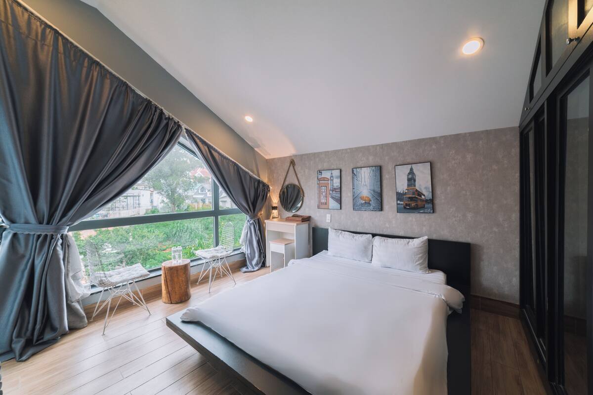 A modern bedroom with a large bed, a desk, and a chair near a window with curtains.