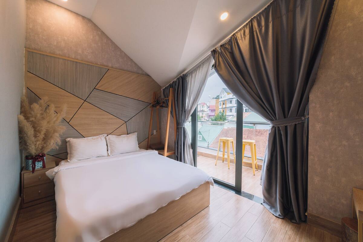 A modern bedroom with a large bed, a wooden headboard, and a view of the city through large windows.