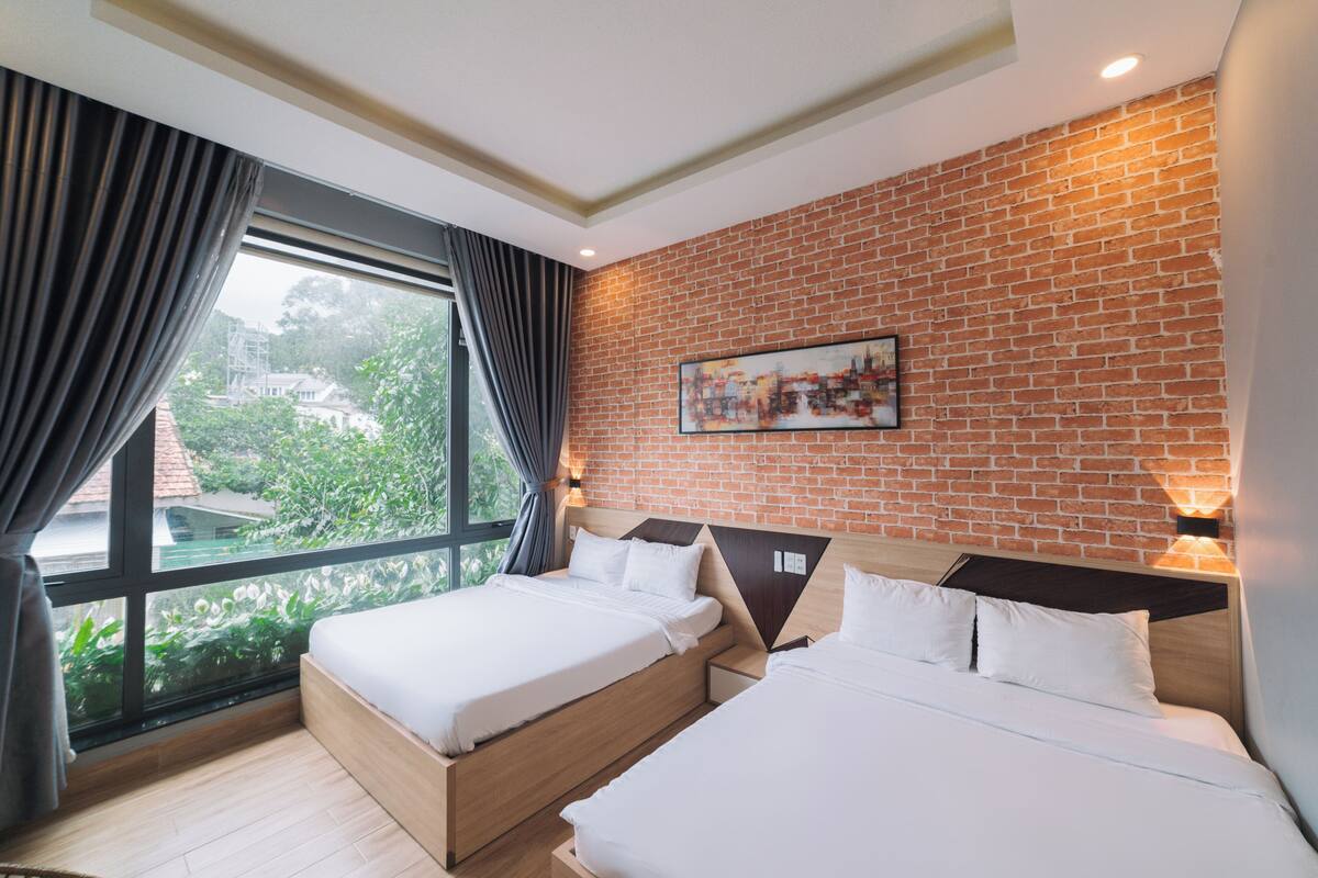 A hotel room with two beds, a brick wall, and a large window with curtains.