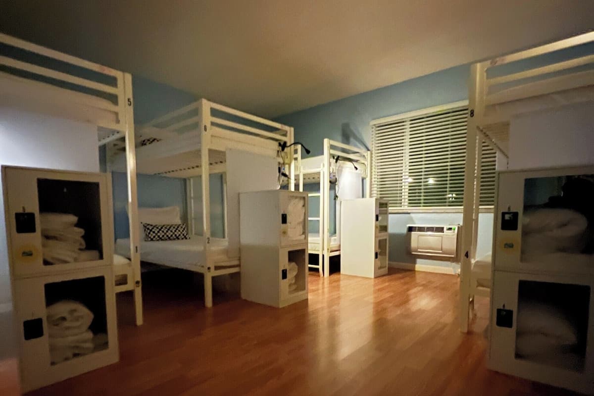 A room with bunk beds, wooden flooring, and a window with blinds.