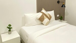 A modern bedroom with a bed, white nightstand, and a wall-mounted lamp. - Hotel H4  (El Paraíso)