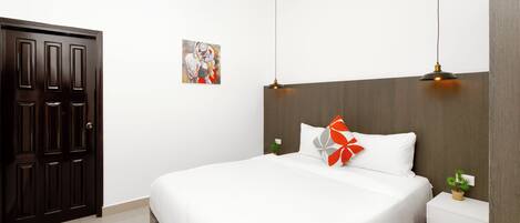 Ein Schlafzimmer mit einem großen Bett, einem Nachttisch, einer kleinen Topfpflanze, einem Wandbild und einem dunklen Holzschrank.