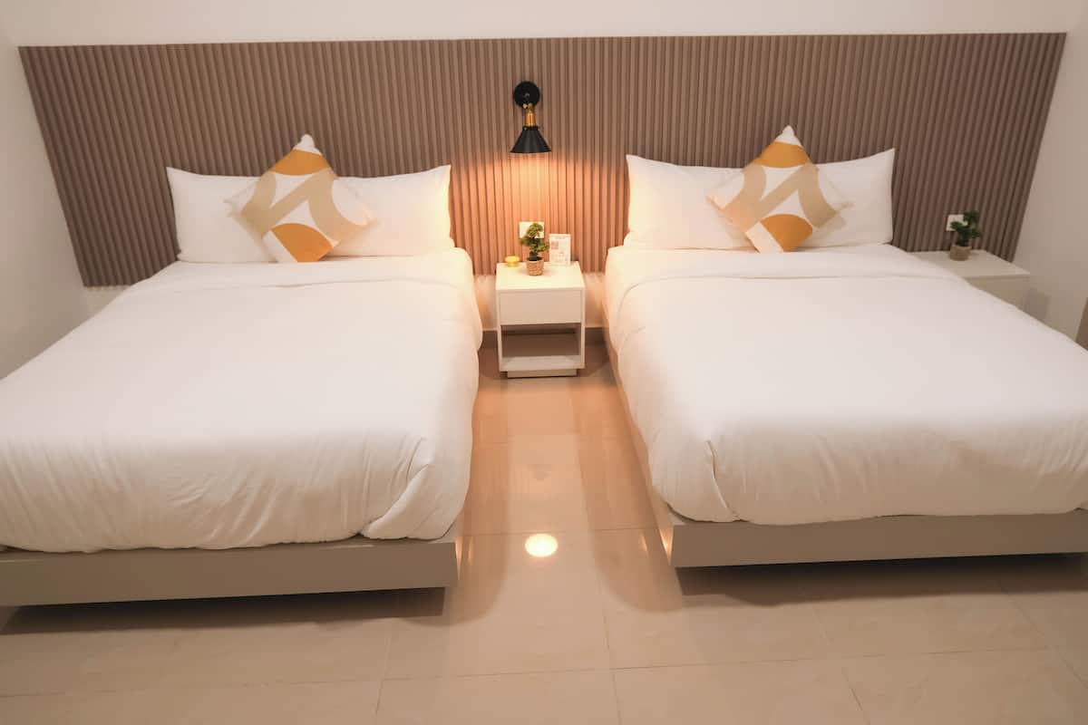 Una habitación de hotel con dos camas, una mesita de noche con lámpara y una planta pequeña.