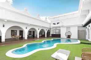 A pool area with a curved design, surrounded by white walls and green artificial grass.
