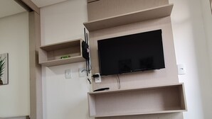 Une chambre d’hôtel avec un téléviseur à écran plat fixé à un mur en bois, une prise de courant et une télécommande posée sur une étagère. Des serviettes blanches pliées sont disposées sur le lit.
