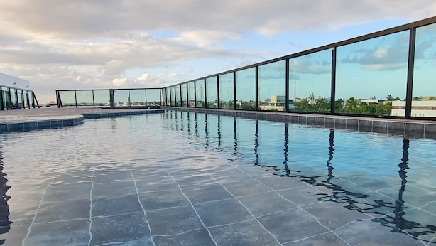 Une piscine dotée d’une paroi en verre et d’un sol carrelé, entourée d’un ciel dégagé.