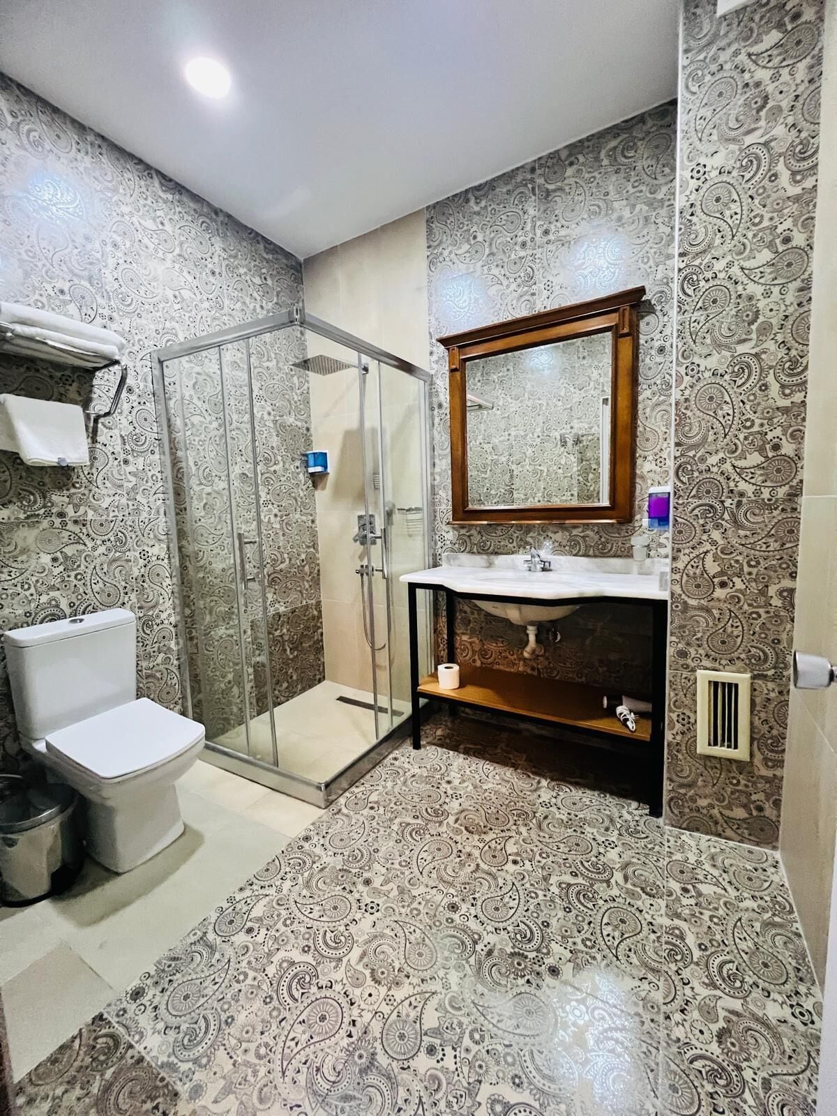 A bathroom with a toilet, a glass-enclosed shower, a vanity with a mirror, and patterned walls.