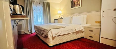 Une chambre d’hôtel avec un lit, un bureau, une lampe, un tableau au mur et une moquette rouge.