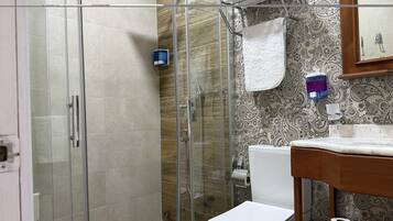 Un bany amb plat de dutxa de vidre, un vàter i un lavabo amb mirall a la part superior.