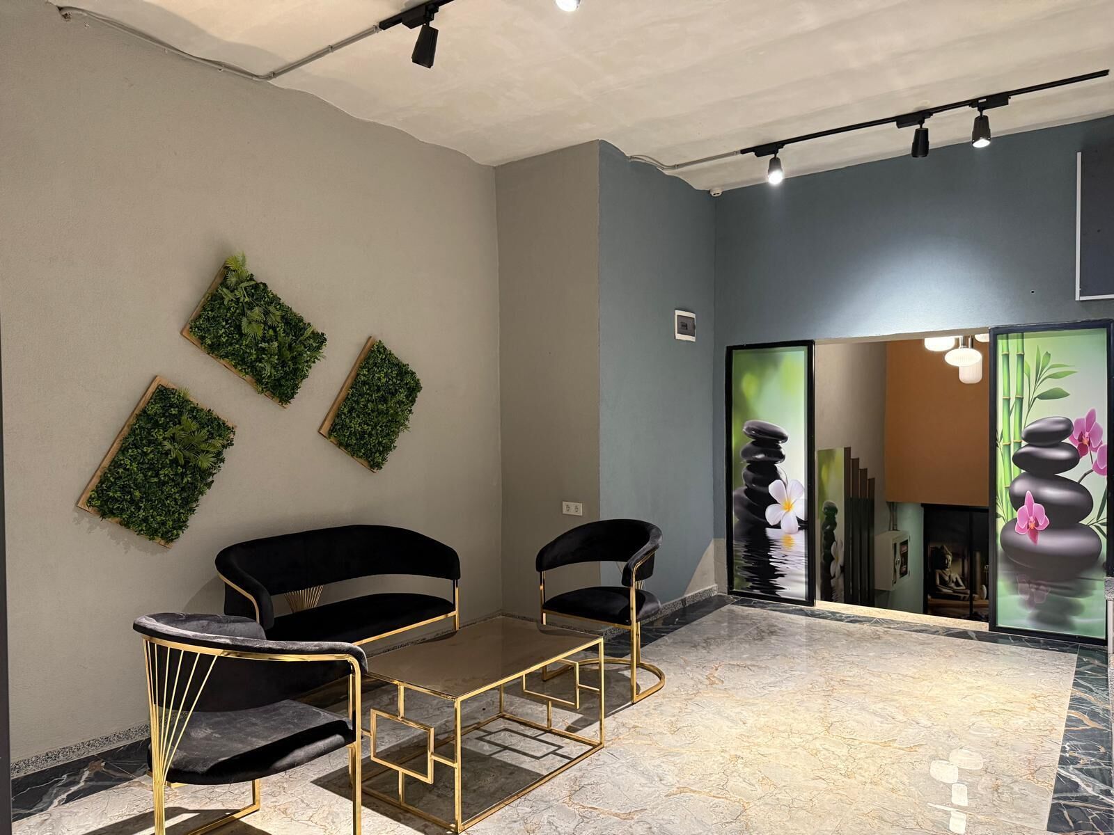 A modern room with a glass partition, two black chairs with gold frames, a small table, and green wall decorations.