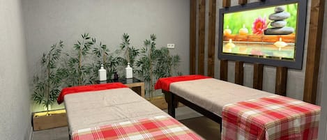Una stanza spa con due lettini da massaggio, un condizionatore d'aria a parete e un televisore che mostra una scena naturalistica.