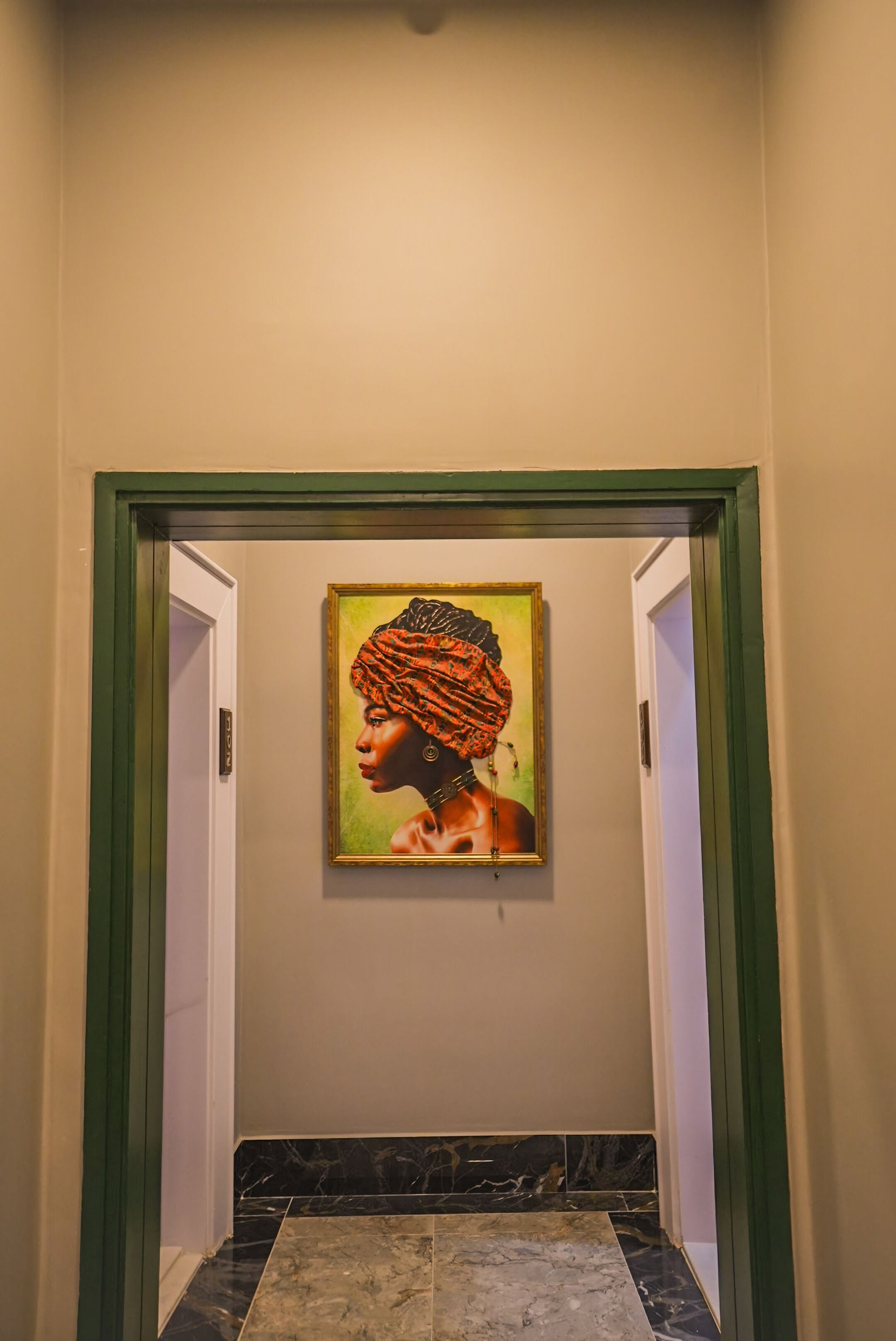 A hallway with a framed artwork on the wall, a green-framed door, and a marble floor.