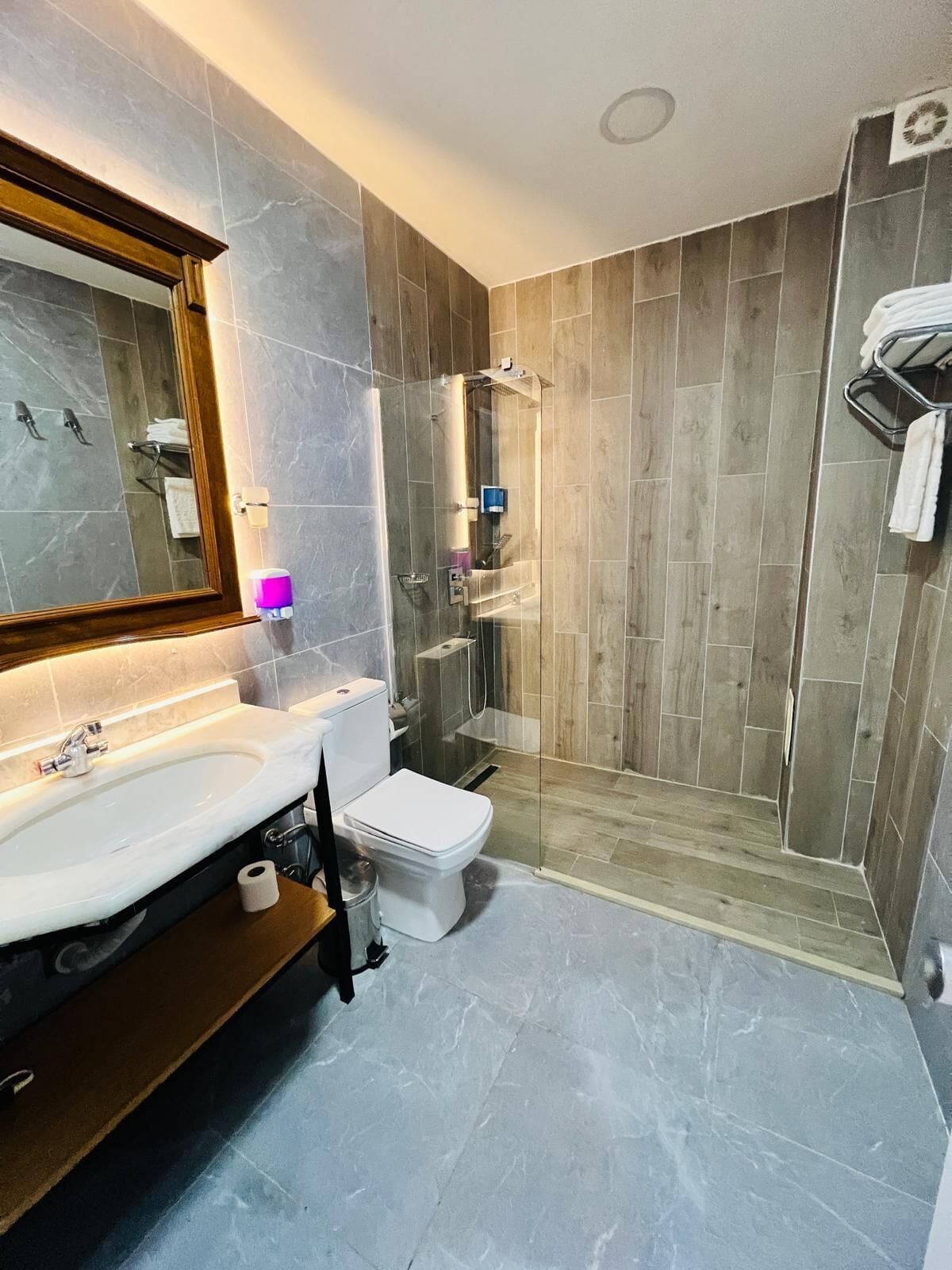 Een moderne badkamer met een marmeren wastafel, toilet en een douchecabine met glazen wanden.