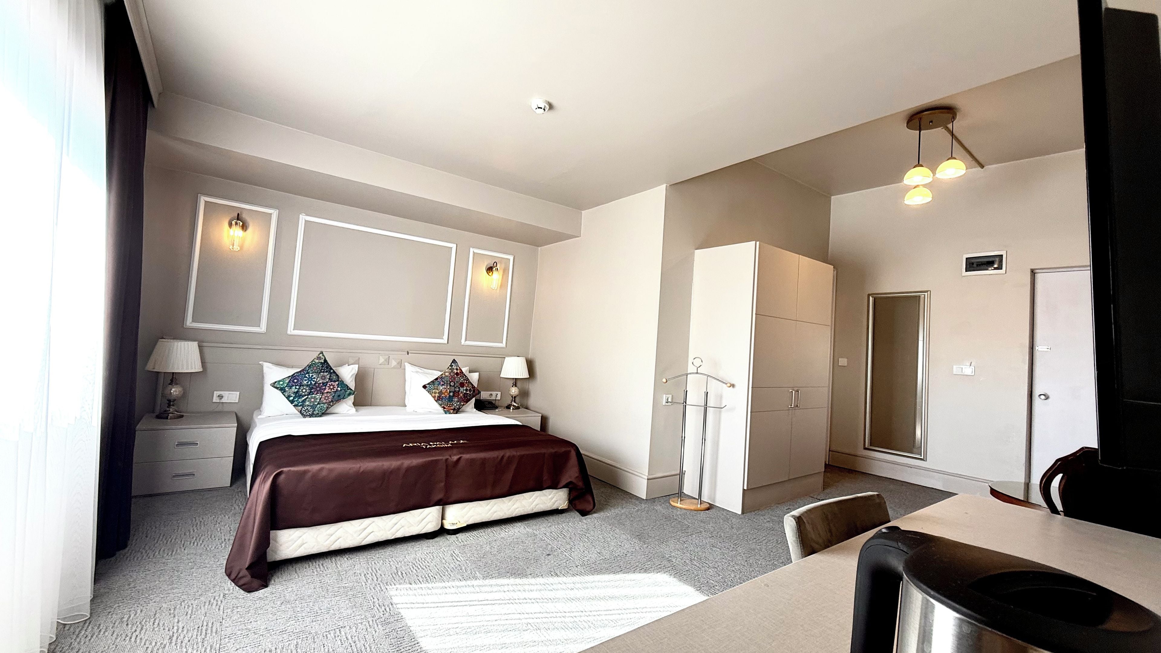 Una habitación de hotel con cama, mesitas de noche, escritorio, silla, armario y espejo.