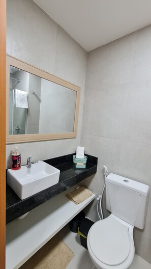 A bathroom with a white sink, a mirror, a toilet, and a black countertop.