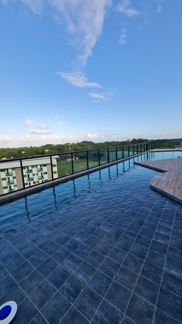 A rooftop infinity pool with a clear view of a residential area and greenery in the background.
