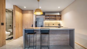 Cocina moderna con una isla central, dos taburetes de bar, armarios de madera y una lámpara colgante.