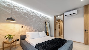 Un dormitorio moderno con una cama grande, una mesita de noche con una planta, una lámpara colgante y un armario.