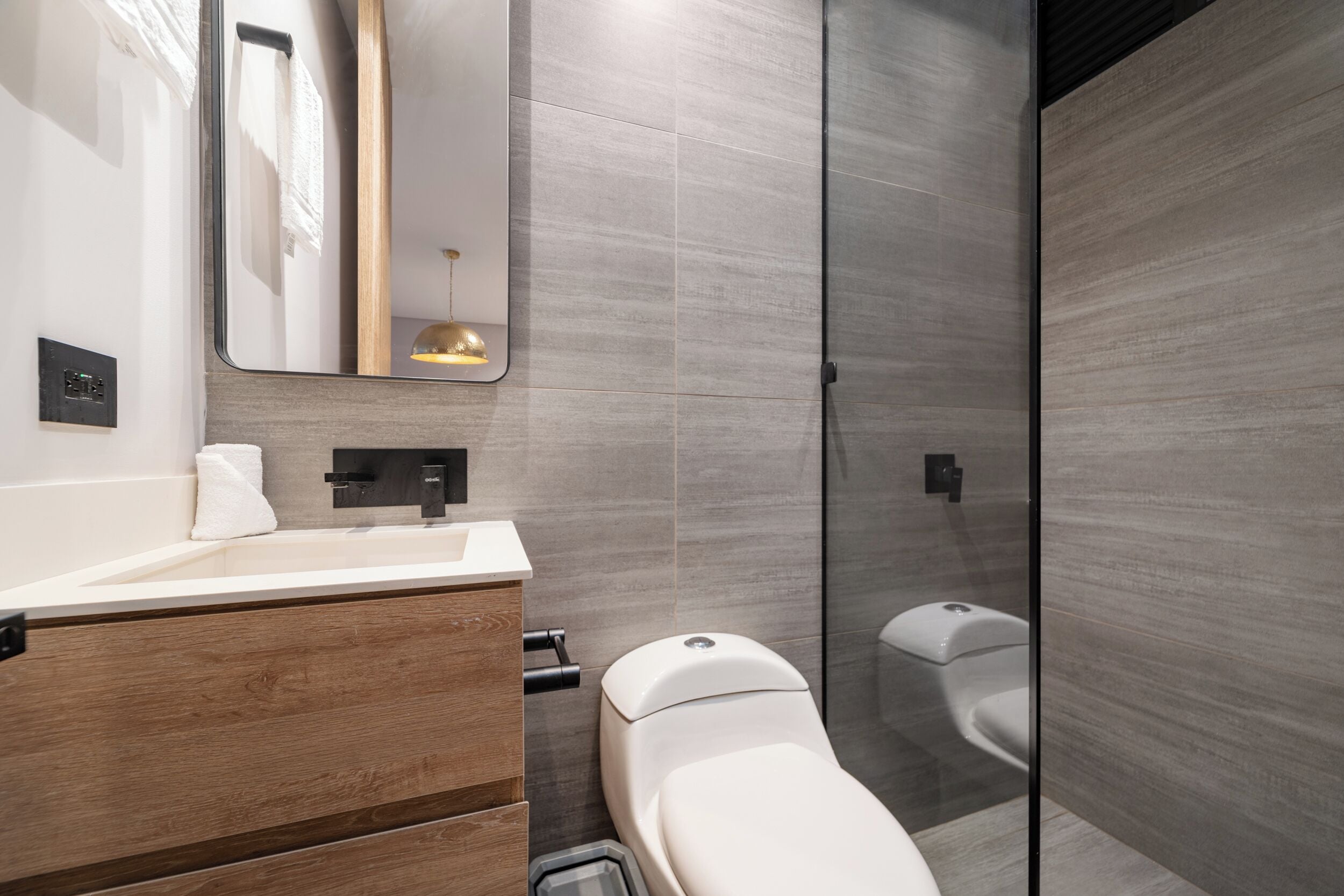 Een moderne badkamer met een houten wastafelmeubel, toilet en een douchecabine van glas.