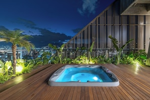 Een hottub op een houten terras met uitzicht op de stad 's nachts.