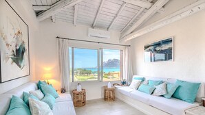 Ein Zimmer mit einem weißen Sofa, türkisfarbenen Kissen, Korbwannen und Meerblick.
